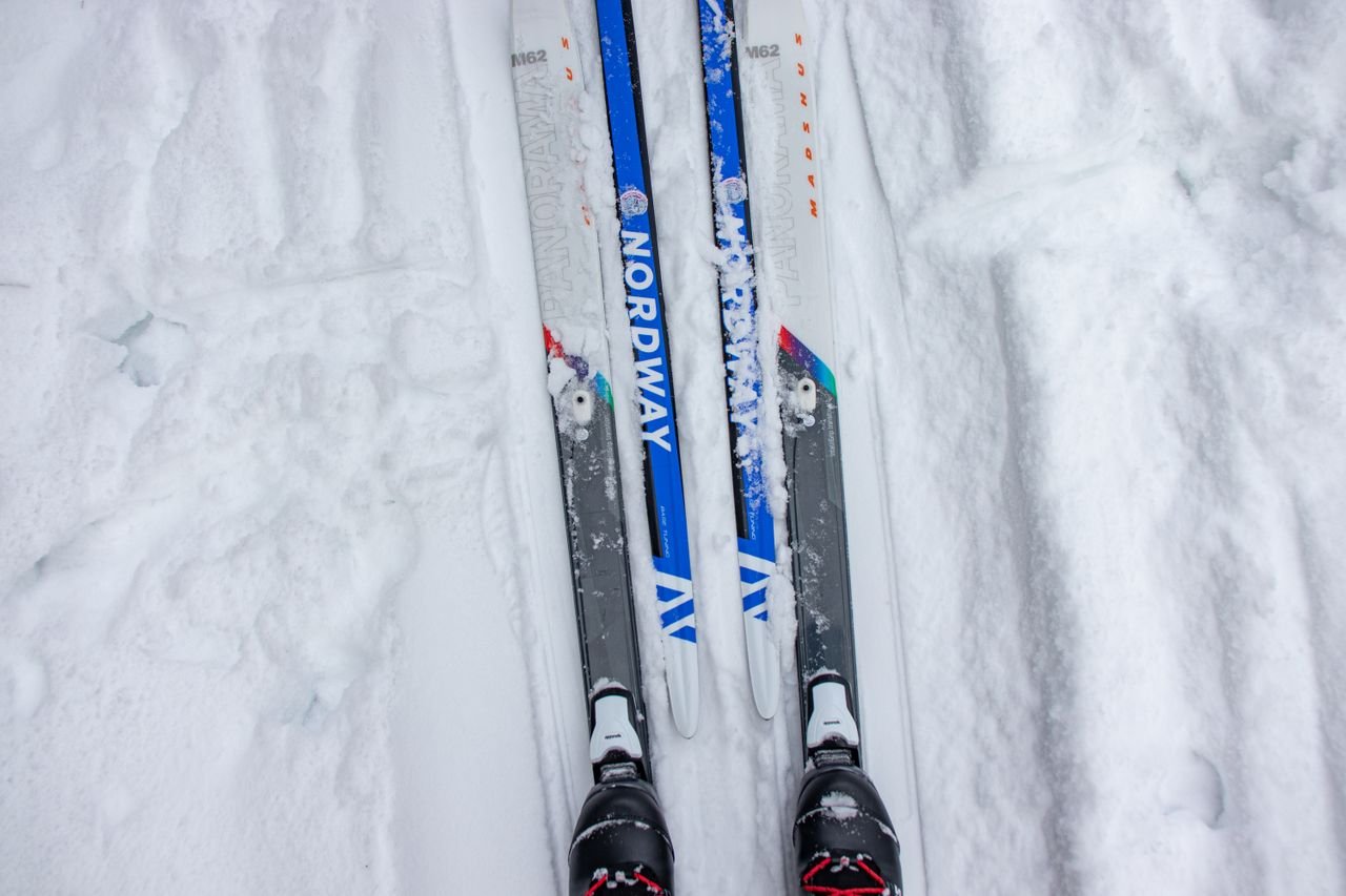 why-choose-us-02 Top view of cross-country skis on a snowy trail in a winter setting, perfect for outdoor sports enthusiasts.