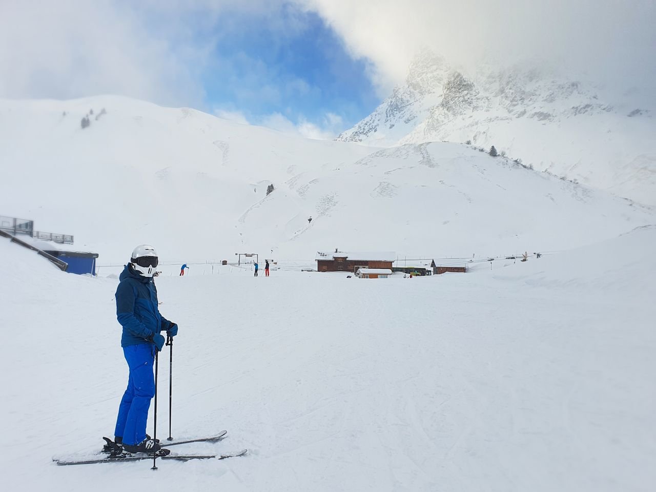 about-03 A skier pauses to admire the snow-capped mountains under a clear blue sky at a ski resort.